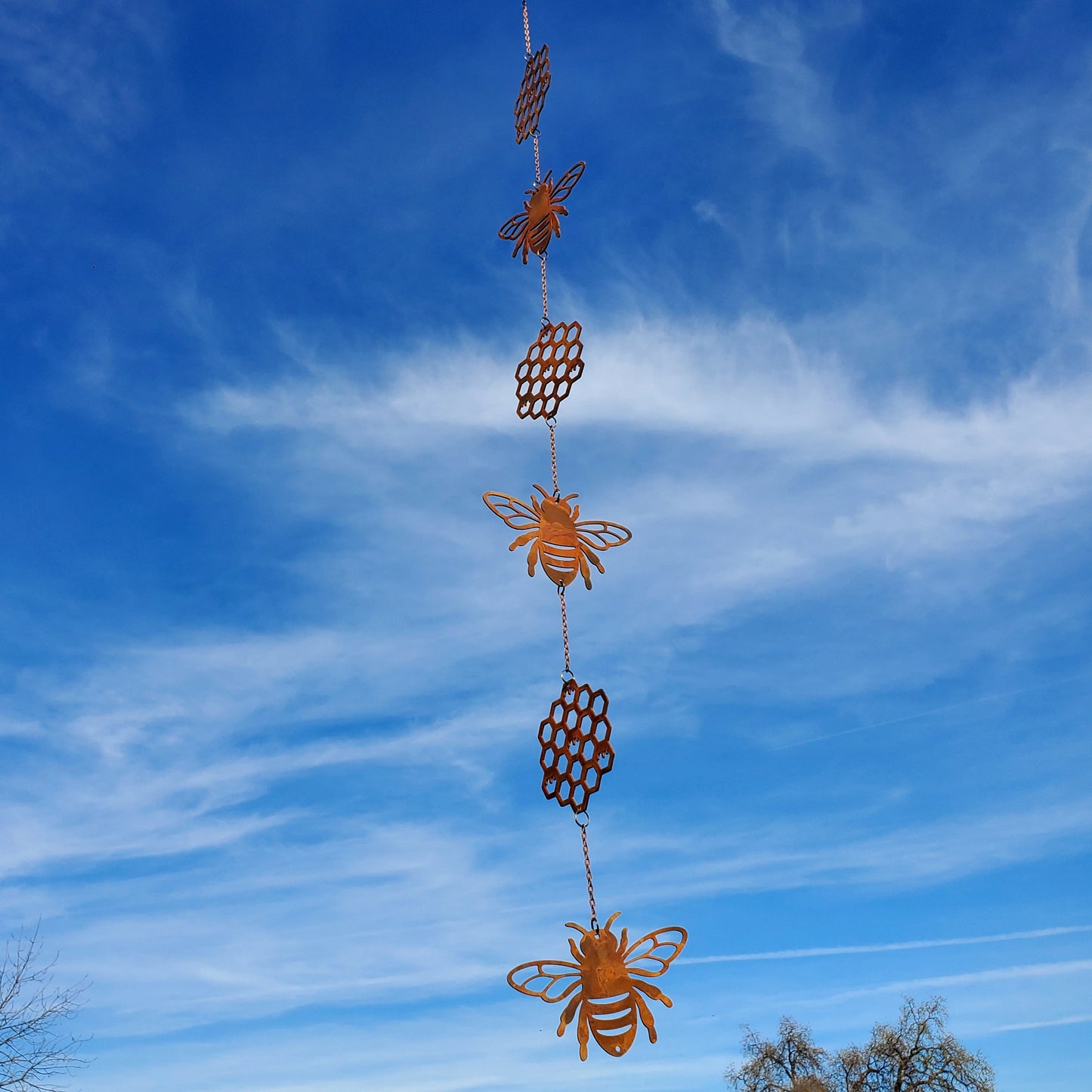 Bee honeycomb wind spinner spinning in the breeze outdoors, hanging in a garden or porch setting with natural background