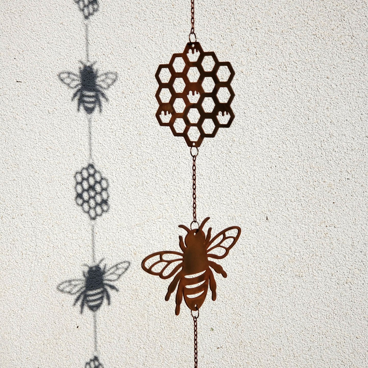 Decorative hanging windchime with bee and honeycomb design on a textured white background