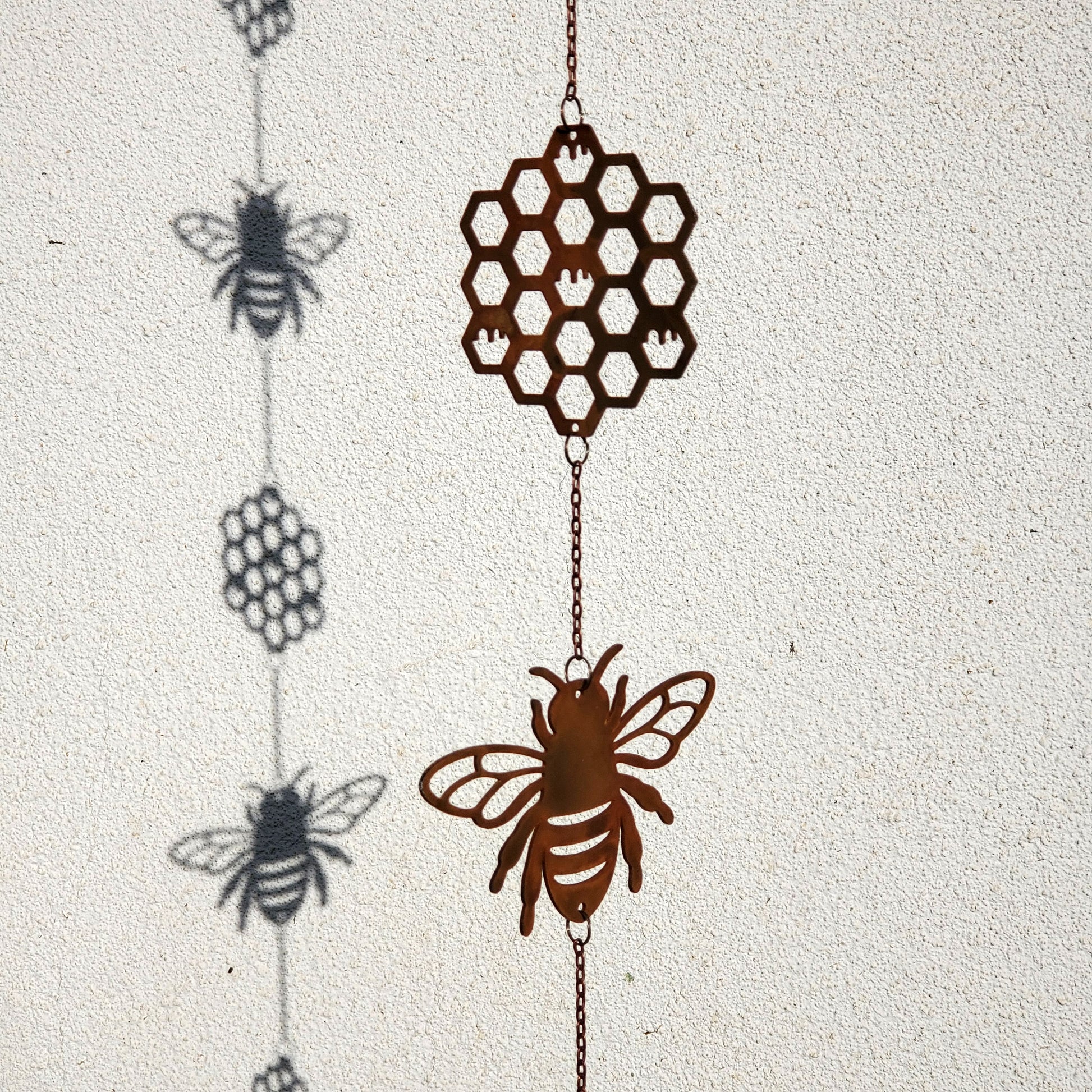Decorative hanging windchime with bee and honeycomb design on a textured white background