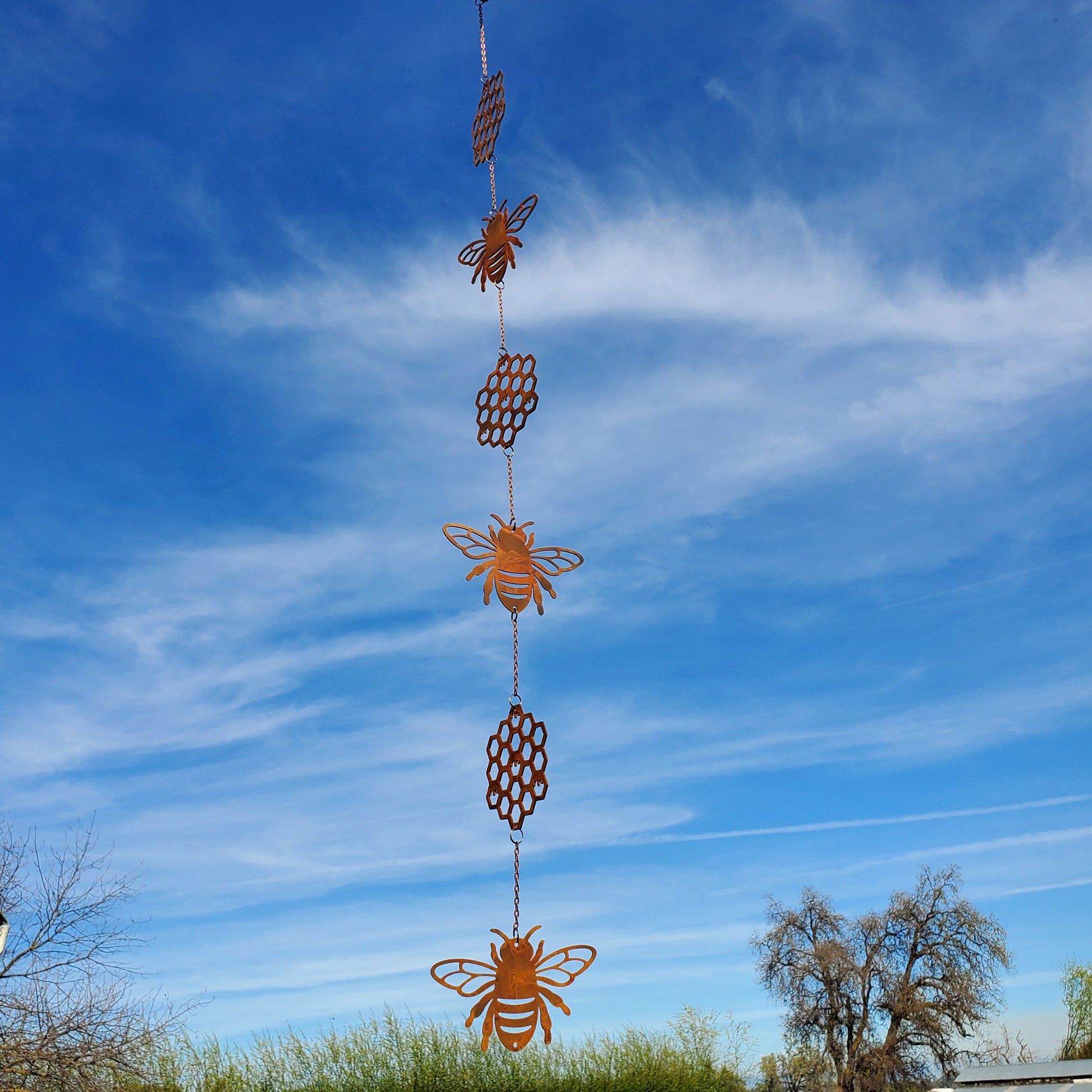 Decorative hanging wind spinner  with bees and honeycomb shapes against a blue sky.